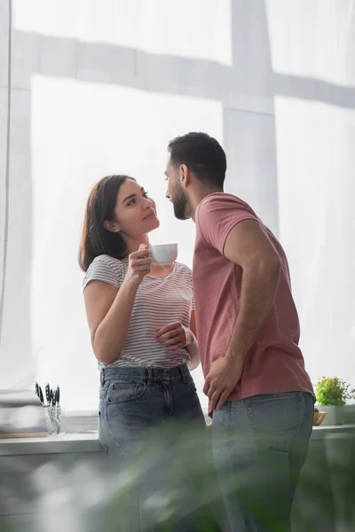 笑顔若いです若いです女性とともにホワイトコーヒーカップ立っていますとともにボーイフレンドで現代的なキッチン — ストック写真