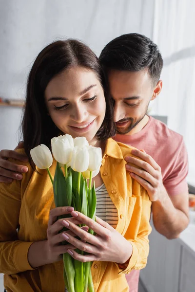 Lächelnder Junger Mann Umarmt Freundin Mit Blumenstrauß Küche — Stockfoto