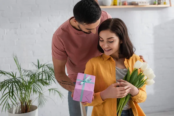 Jovem Apresentando Caixa Presente Para Namorada Com Buquê Flores Cozinha — Fotografia de Stock