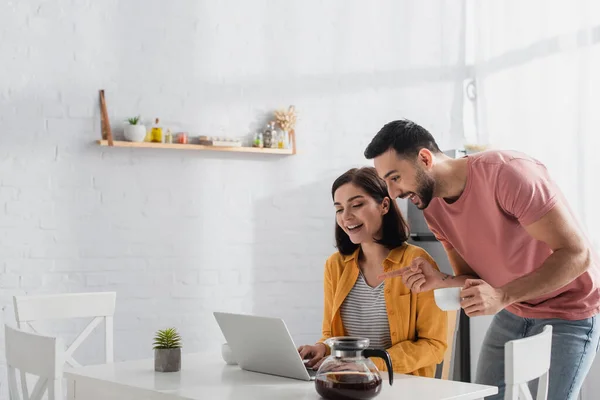 Joven Apuntando Con Dedo Computadora Portátil Cerca Novia Sonriente Cocina —  Fotos de Stock