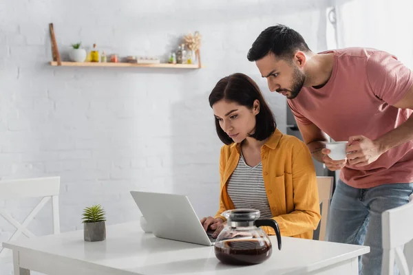 Serious Young Man Drinking Coffee Looking Laptop Girlfriend Kitchen — 스톡 사진