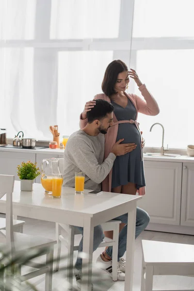 年轻男子在厨房里摸着一个笑着的孕妇的肚子 — 图库照片