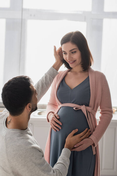 young man touching belly and face of pregnant woman in kitchen