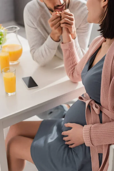 在厨房里 一个拿着手机坐在桌旁 牵着怀孕妇女的手的年轻人的半影 — 图库照片