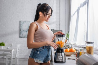 Genç esmer kadın dilimlenmiş portakallarla karıştırıcı sürahiye bakıyor.