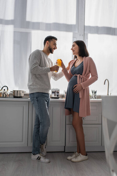 happy young man and pregnant woman standing with orange juice in kitchen