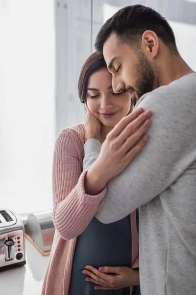 Glücklicher Junger Mann Mit Geschlossenen Augen Umarmt Schwangere Frau Küche — Stockfoto