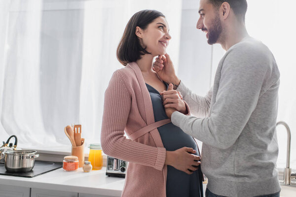 happy young man touching face of pregnant woman in kitchen