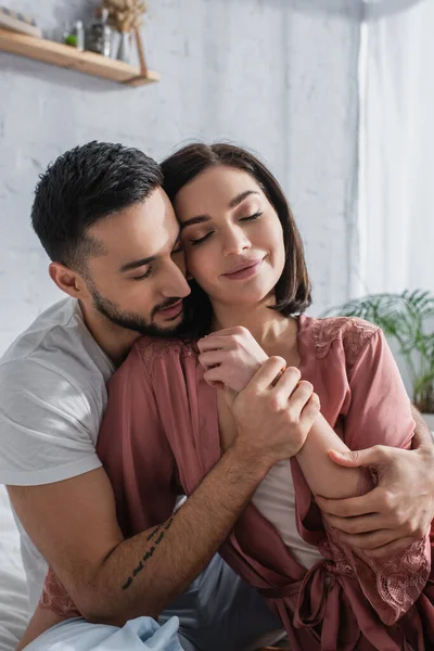 Mladý Muž Dotýkání Ruky Přítelkyně Peignoir Zavřenýma Očima Ložnici — Stock fotografie