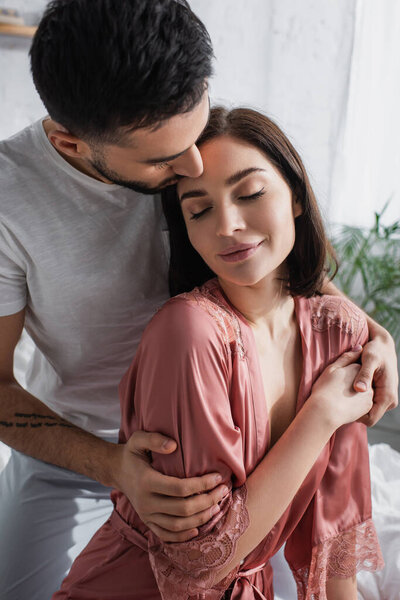 smiling young couple with closed eyes gently hugging in bedroom