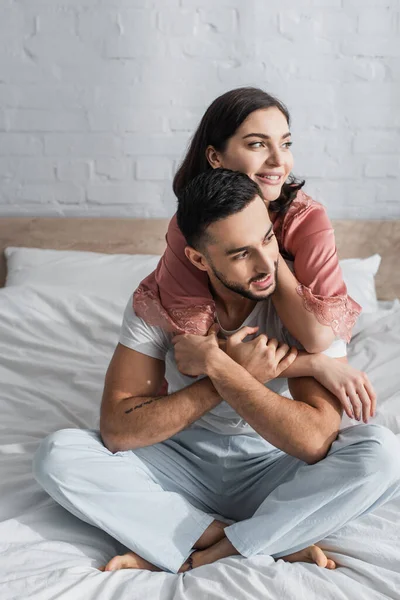 积极的年轻夫妇坐在床上 头戴白色亚麻布 抱在卧室里 — 图库照片