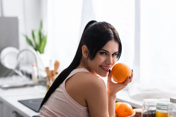 Cheerful Young Woman Holding Orange Looking Camera Kitchen — Stock Photo, Image