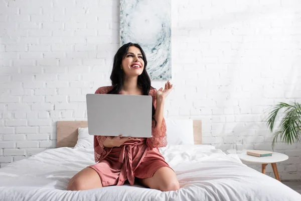 穿着丝绸长袍的快乐的年轻女人拿着笔记本电脑在卧室里 — 图库照片