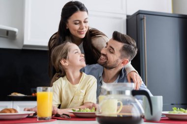 Mutfakta kahvaltıda gülümseyen mutlu aile ön planda bulanık.
