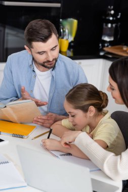 Ödev yapan kızın yanındaki defteri gösteren ebeveynler. 