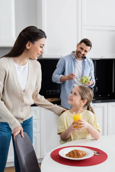 Glimlachend Meisje Met Glas Sinaasappelsap Kijken Naar Mam Buurt Wazig — Stockfoto