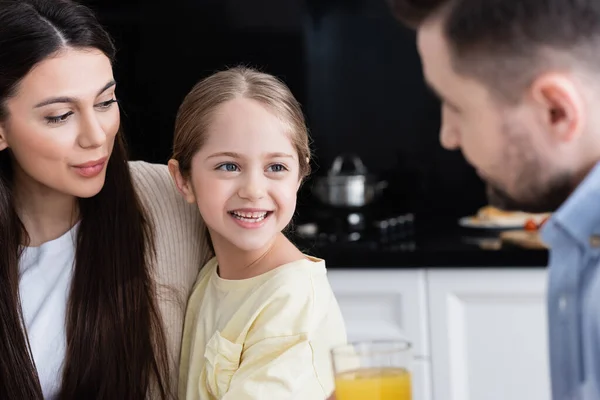 Alegre Chica Sonriendo Cerca Madre Borrosa Padre Con Jugo Naranja — Foto de Stock