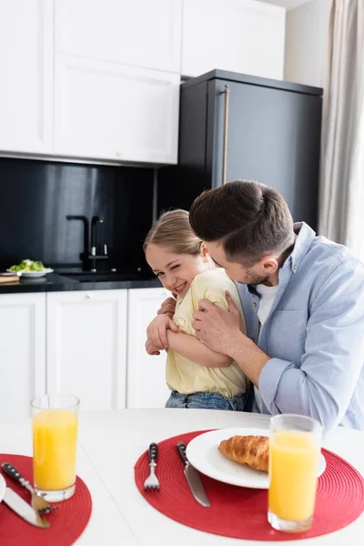 Padre Abbracciando Figlia Allegra Vicino Succo Arancia Croissant Cucina — Foto Stock