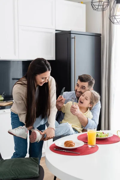 Excitada Chica Sosteniendo Tenedor Cuchillo Mientras Divierten Con Los Padres — Foto de Stock