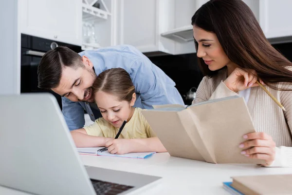 Meisje Schrijven Notebook Buurt Glimlachende Vader Moeder Met Leerboek — Stockfoto