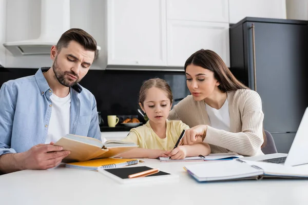 Hombre Leyendo Libro Mujer Señalando Con Dedo Mientras Ayuda Hija —  Fotos de Stock