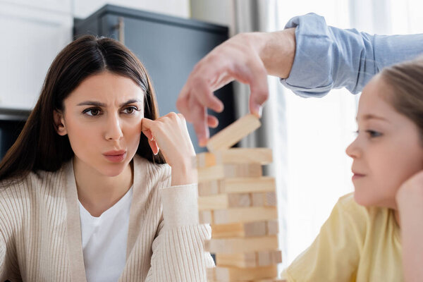 worried woman looking at husband removing block from wooden tower, blurred foreground