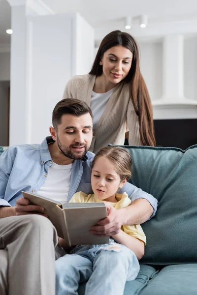 Mujer Mirando Marido Hija Leyendo Libro Juntos Casa — Foto de Stock