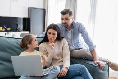 Mutlu kız kanepenin yanındaki dizüstü bilgisayarı işaret ediyor.