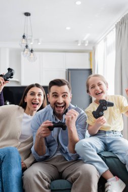 KYIV, UKRAINE - 8 Nisan 2021: heyecanlı aile evde joysticklerle oynarken kazanma hareketi gösteriyor
