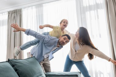 Mutlu ebeveynler evde kızlarıyla oynarken uçuşu taklit ediyorlar.