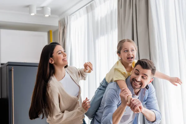 joyful child piggybacking on fathers back near cheerful mother