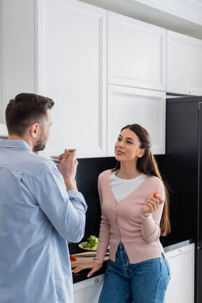 キッチンで夫の試食会を見て笑顔の女性 — ストック写真