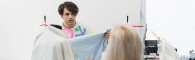 fashion designer showing sample of textile to colleague on blurred foreground, banner clipart