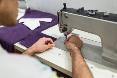 Atölyede çalışırken dikiş makinesi kullanan bulanık terzinin kırpılmış görünümü
