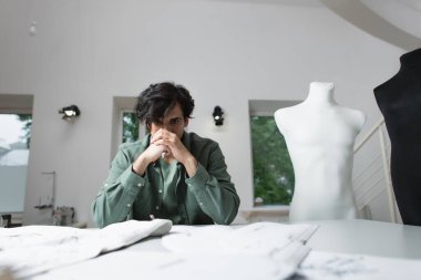 Düşünceli terzi atölyede bulanık dikiş desenleri ve dokuların yanında oturuyor.