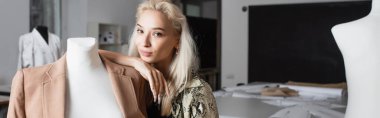 Manken ve pankartın yanındaki kameraya gülümseyen genç moda tasarımcısı.