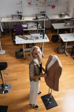 high angle view of fashion designer near mannequin and sewing machines in atelier clipart