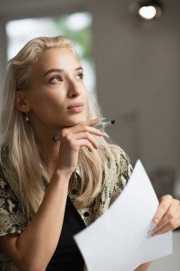 dreamy fashion designer with paper and felt pen looking away in atelier clipart