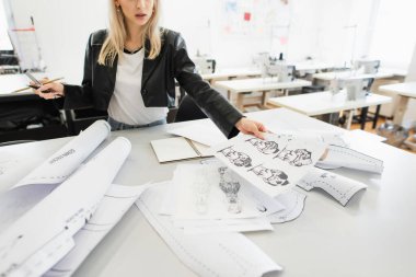 Atölyede çalışırken elinde çizimler tutan moda tasarımcısının kırpılmış görünümü