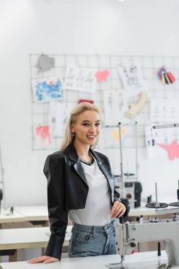 Moda atölyesinde dikiş makinesinin yanındaki kameraya bakan güzel bir moda tasarımcısı.