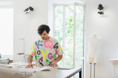 Moda tasarımcısı atölyedeki çizimlere ve dikiş kalıplarına bakıyor