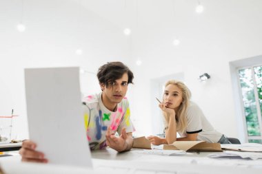 Moda atölyesindeki genç meslektaşına kağıt gösteren moda tasarımcısı