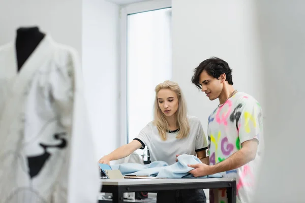 couple of young designers choosing colors and fabric near mannequin on blurred foreground