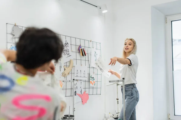 Blonde Fashion Designer Pointing Finger Sketches Blurred Colleague — Stock Photo, Image