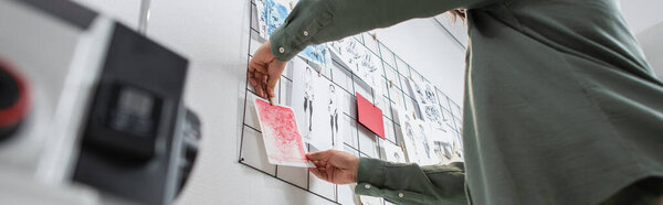 низкоугловой вид срезанный модельер прикрепляя рисунки на стене в ателье, баннер
