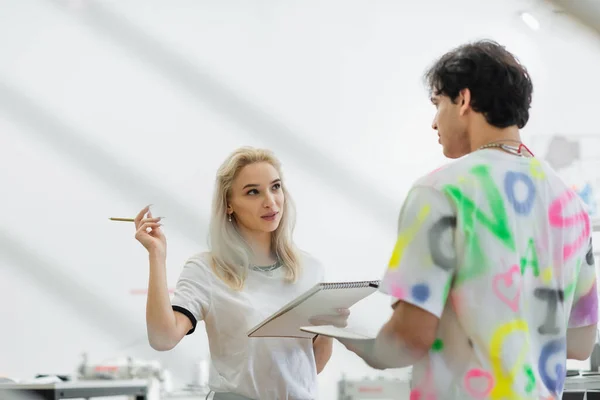 Blondynka Projektant Trzyma Ołówek Podczas Rozmowy Kolegą Moda Atelier — Zdjęcie stockowe