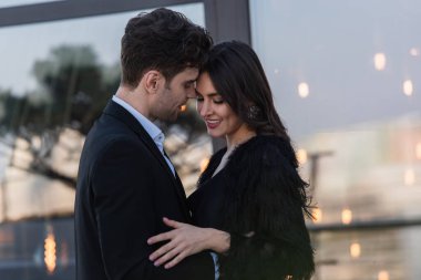 Sahte kürk ceketli mutlu kadın dışarıda takım elbiseli adamı kucaklıyor. 