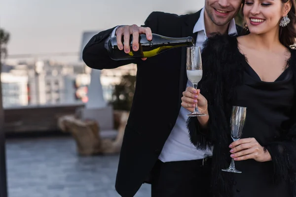 快乐的男人把香槟酒倒在穿着假皮夹克的女朋友的杯子里 — 图库照片