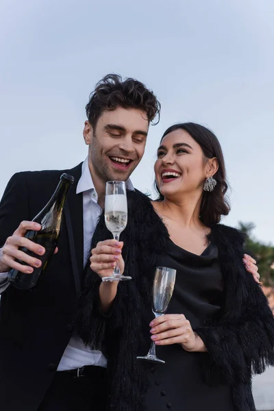 Homem Feliz Segurando Garrafa Champanhe Perto Namorada Animada Casaco Pele — Fotografia de Stock