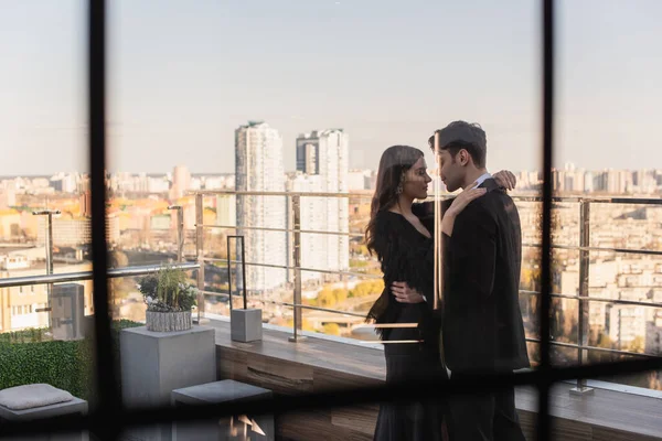 在模糊的餐厅橱窗后面的阳台上拥抱的情侣的侧视图 — 图库照片
